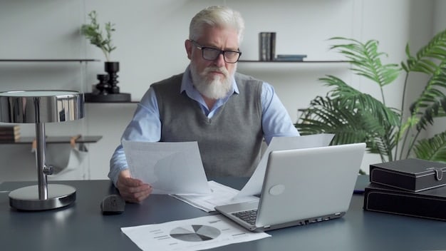 A senior person sitting at a desk reviewing financial documents with a concerned expression, highlighting the importance of Social Security benefits for financial security in retirement.