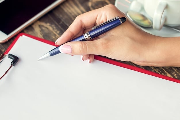Close-up shot of a hand filling out a grant application form with a pen. The form is on a desk cluttered with various documents and a laptop. The background is blurred, bringing focus to the hand and the application.