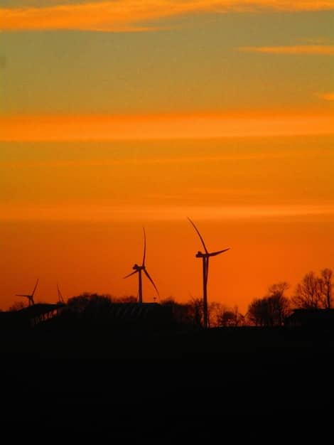 A wind farm at sunset, symbolizing the growth of renewable energy sources and the shift away from fossil fuels.